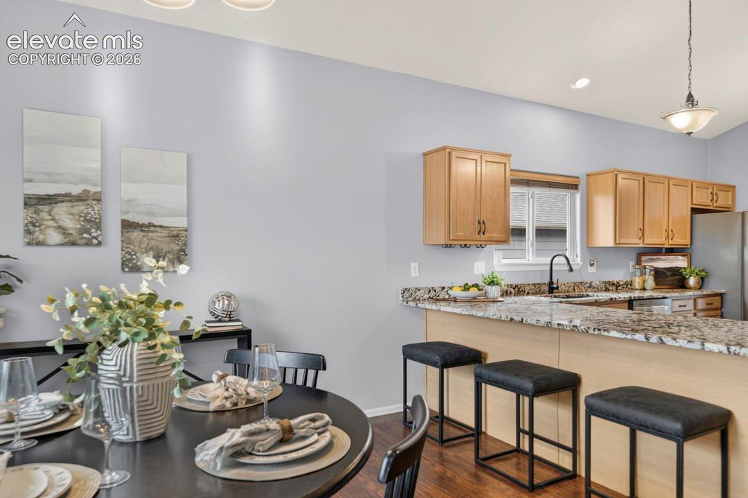 Kitchen featuring stone countertops, wood-finish cabinetry, a high-arc matte black faucet, and a breakfast bar with recessed lighting