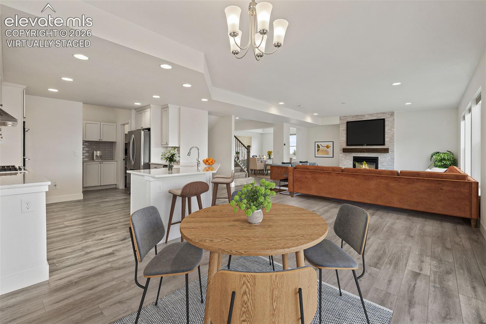 Virtually Staged: Open-concept living space featuring wood-finish LVP flooring, a stone-faced fireplace, recessed lighting, a kitchen island with seating, and white cabinetry