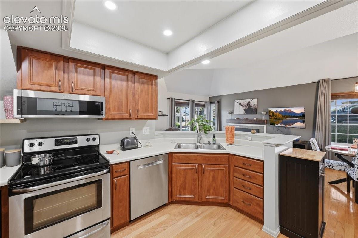 Kitchen featuring recessed tray ceiling lighting, wood cabinetry, stainless steel appliances, neutral countertops, and wood-finish flooring