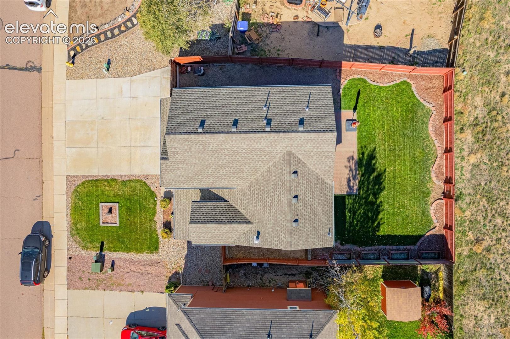 Aerial perspective featuring a multi-pitched asphalt shingle roof, a fenced backyard with a manicured lawn, a concrete driveway, and a detached storage structure