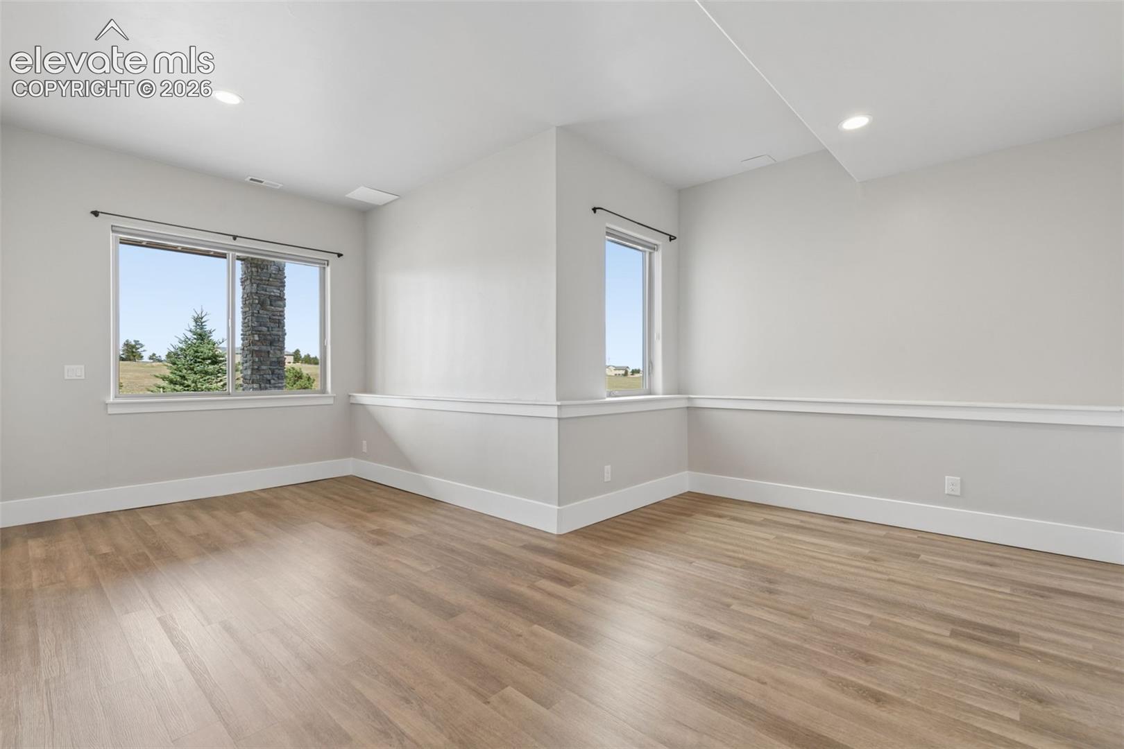 Recessed ceiling lighting, wood-finish flooring, white baseboards, chair rail molding, and multiple windows