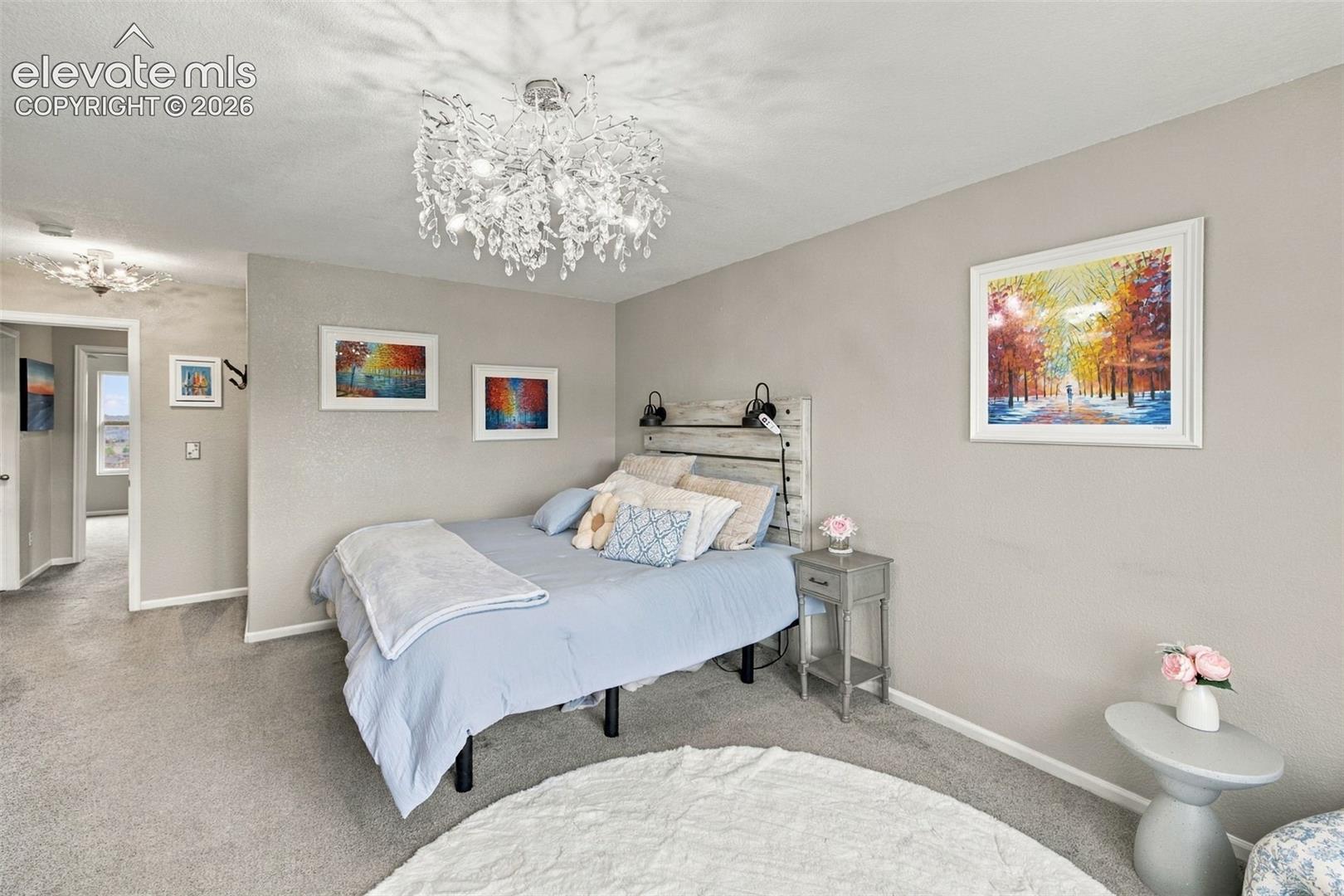 Spacious room featuring neutral carpeting, a statement crystal multi-light chandelier, and a wood-plank accent panel