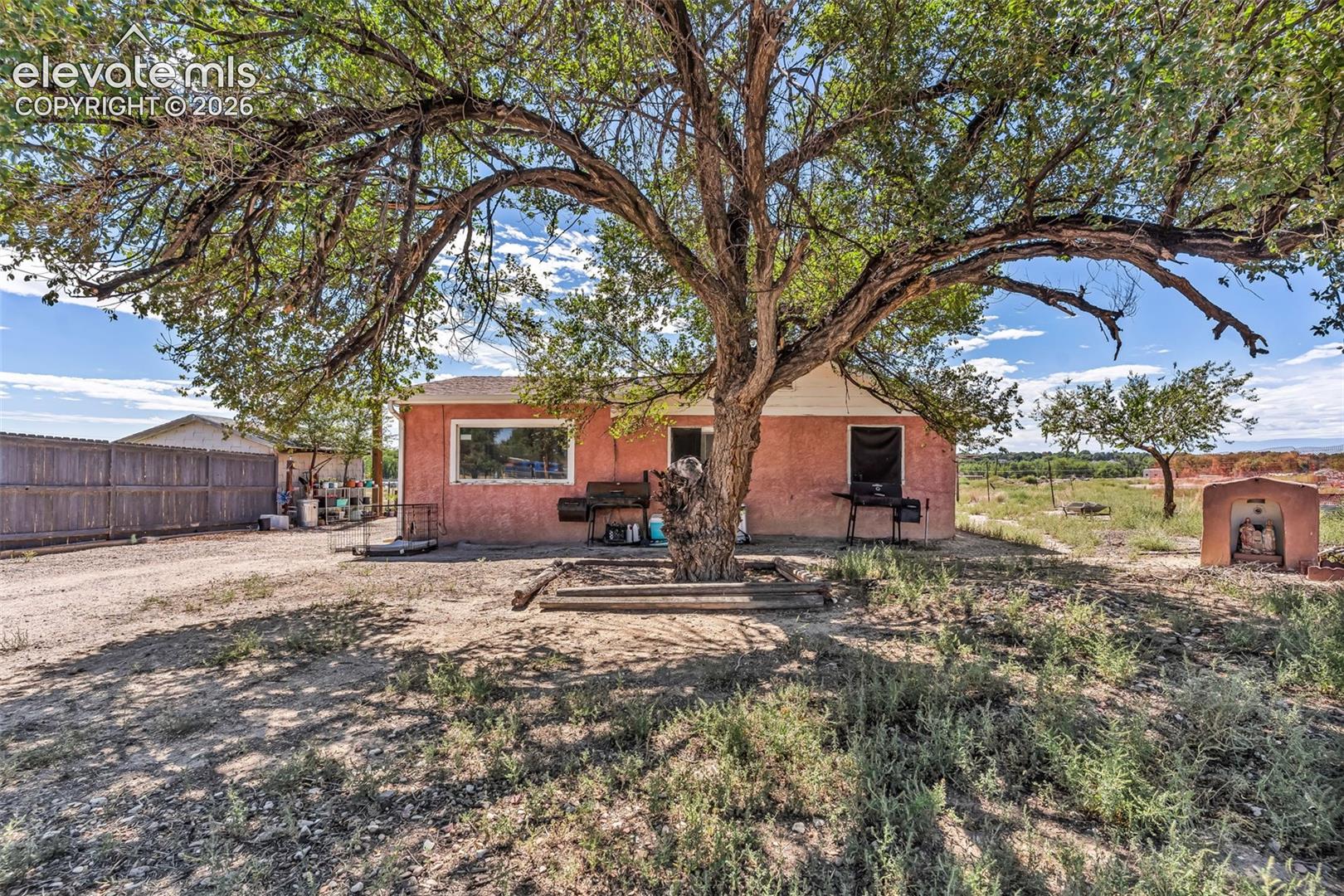 Stucco exterior residence with a prominent mature tree providing natural shade
