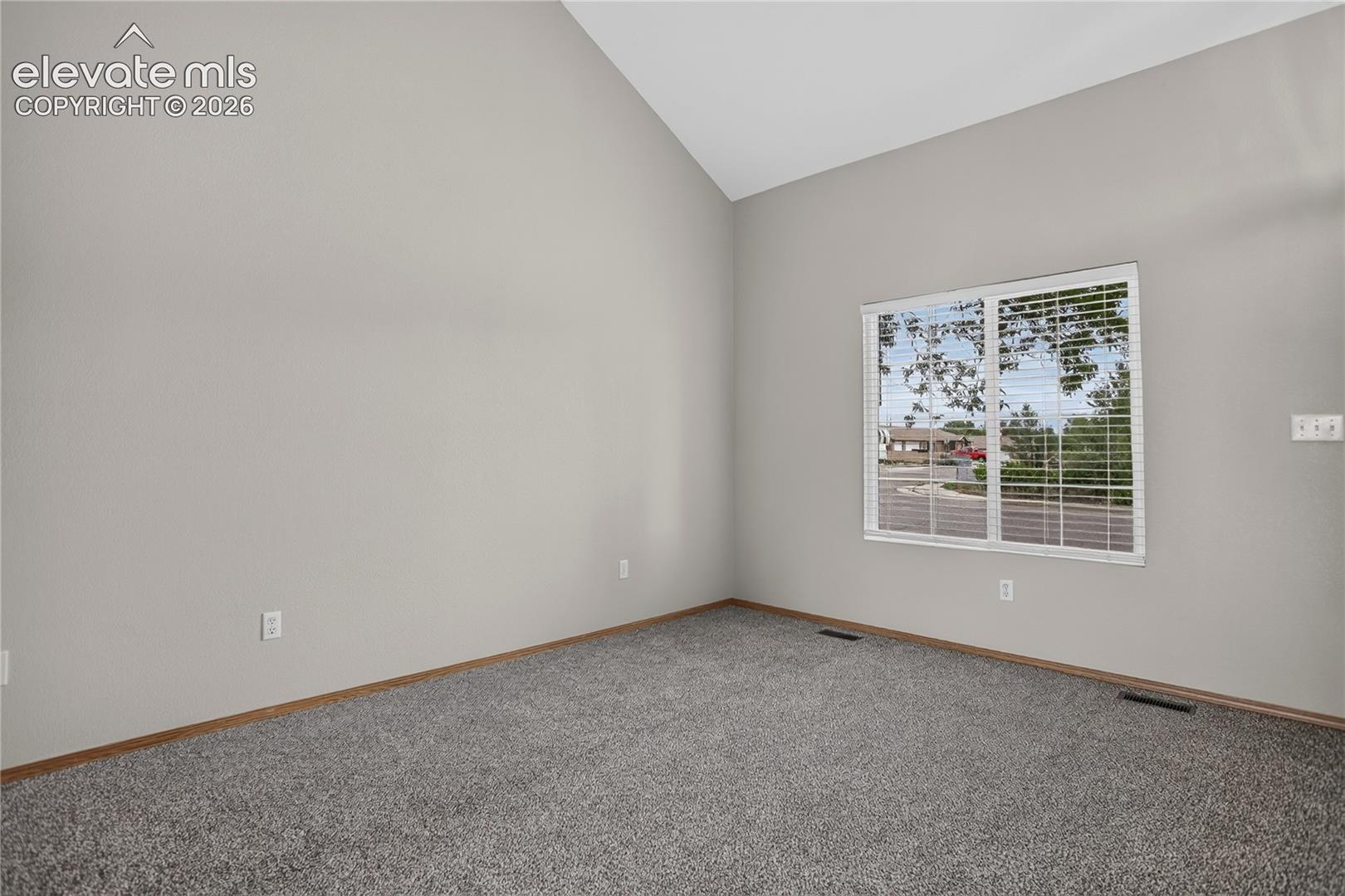 Vaulted ceiling with neutral wall paint and grey carpeting