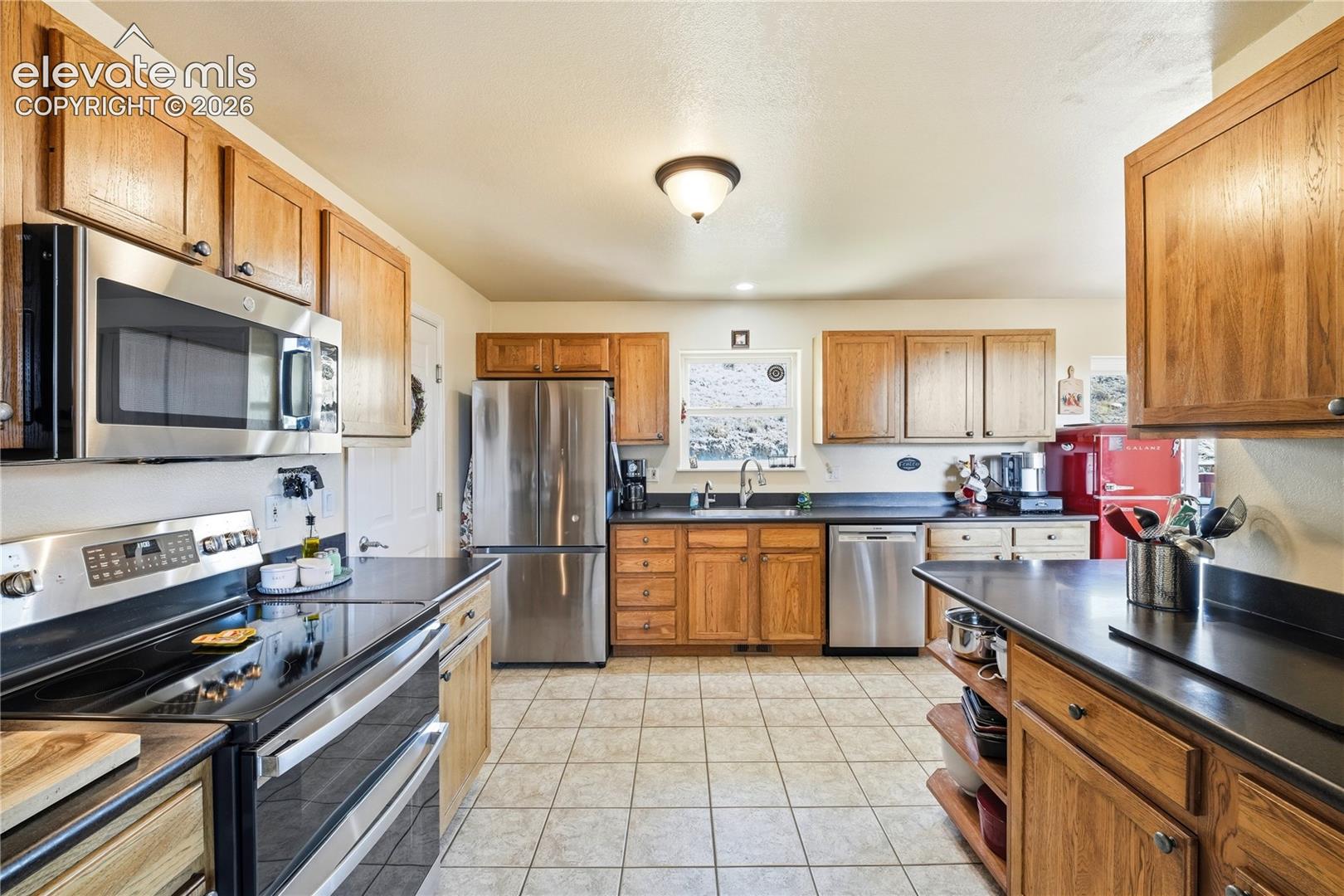 Kitchen featuring tile flooring, wood cabinetry, stainless steel appliances, dark countertops, and a double oven range