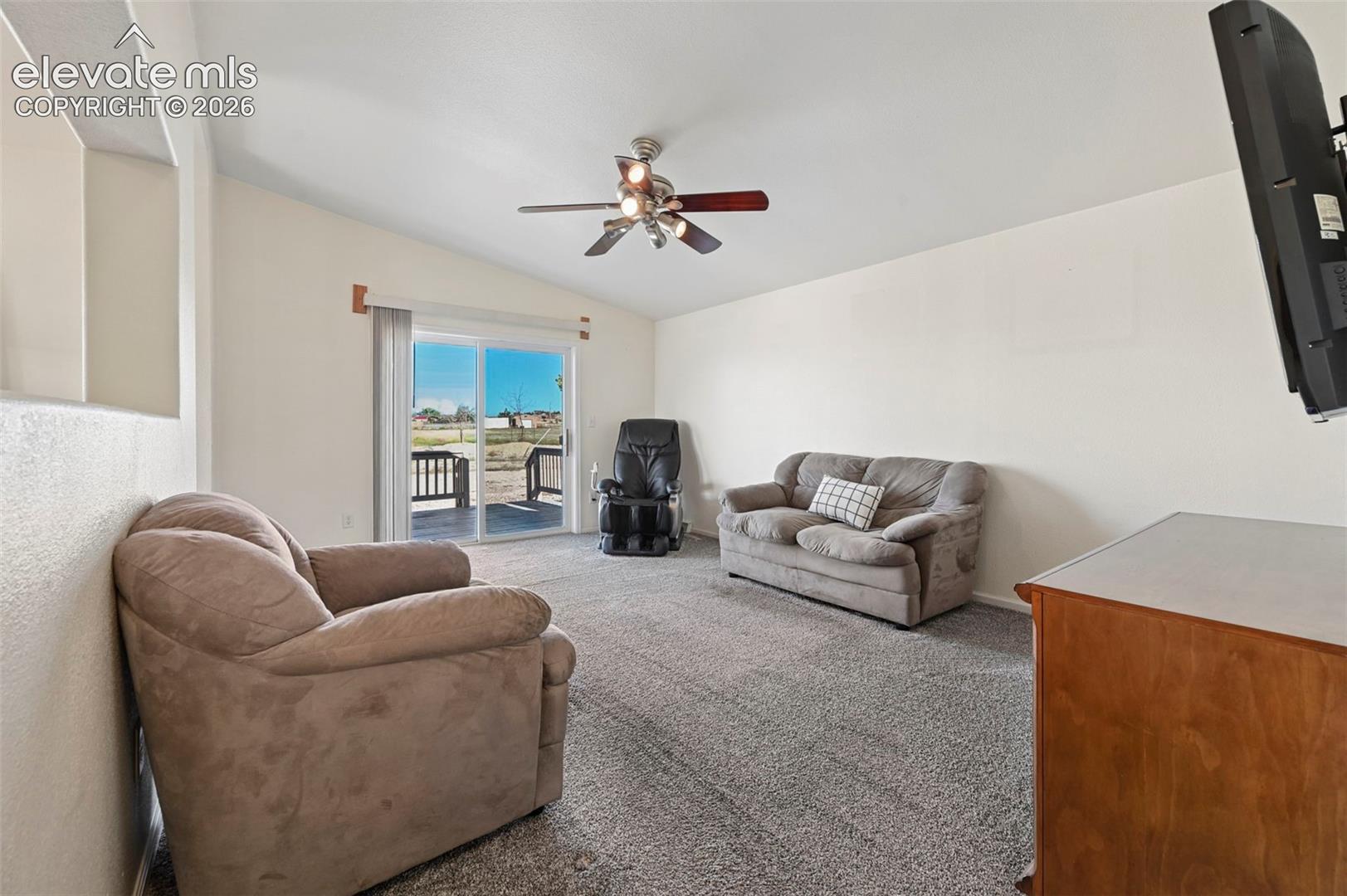 Living area featuring high ceilings, neutral wall tones, plush wall-to-wall carpeting, a multi-blade ceiling fan with integrated lighting, and a sliding glass door