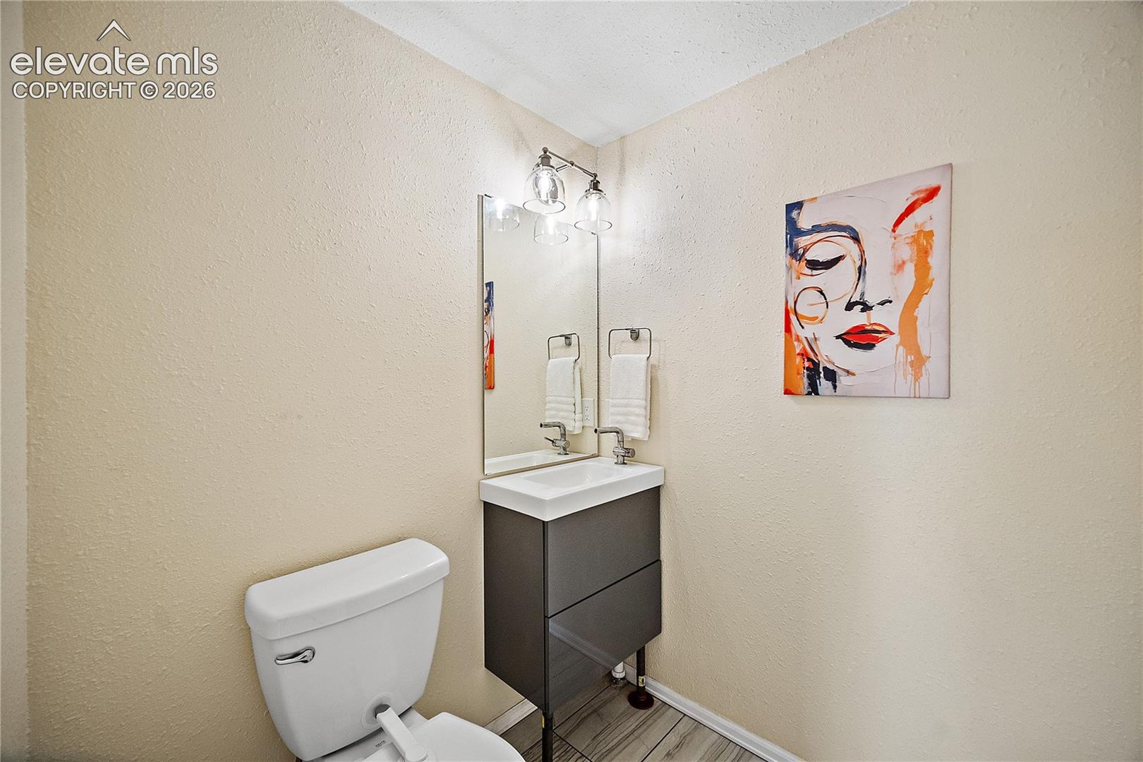 Compact bathroom featuring a white toilet, a modern vanity with a white rectangular sink, a wall-mounted mirror, and overhead vanity lighting