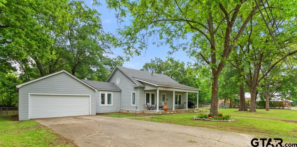 Light gray house with an attached garage and covered porch beneath mature trees.