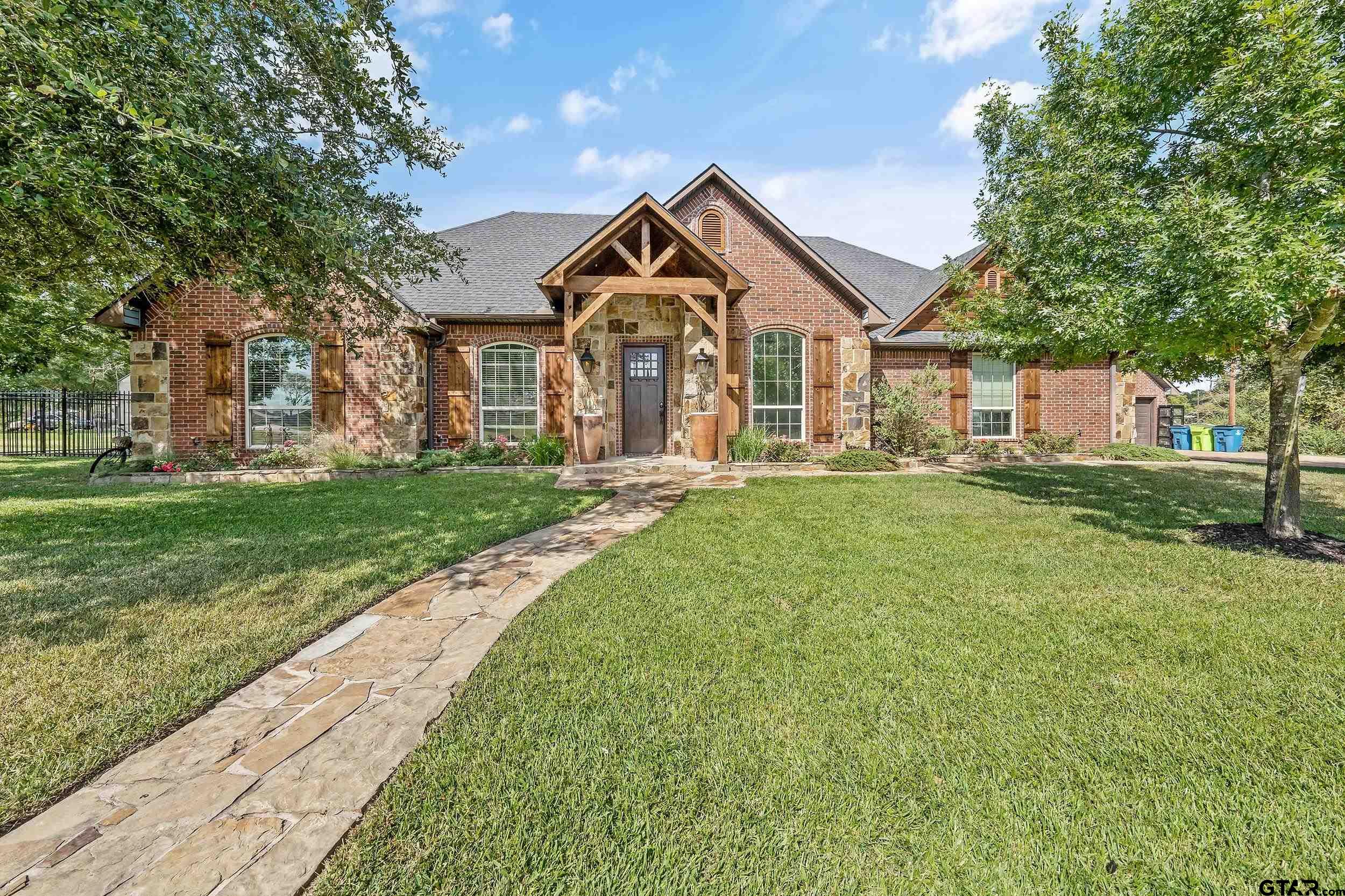 Brick-and-stone home with a timber entry, arched windows, and a stone walkway across the lawn.