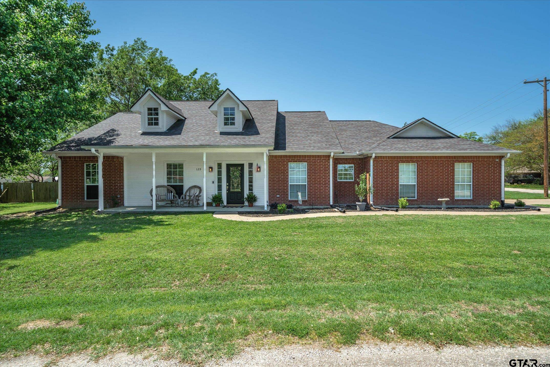 Brick-and-white house with two roof dormers, a covered porch, and a wide front lawn.