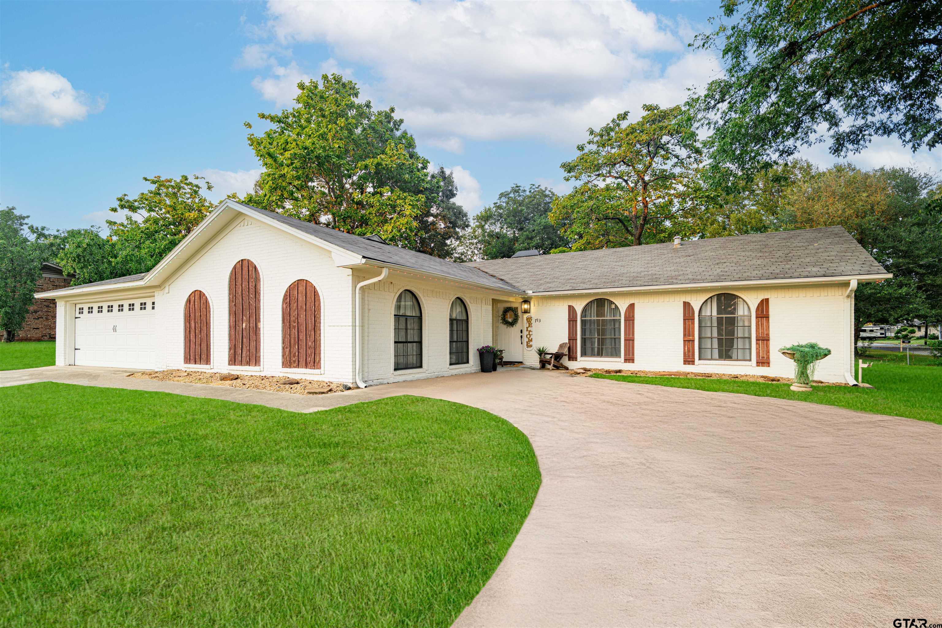 White brick home with arched windows, wooden shutters, attached garage, and broad driveway.