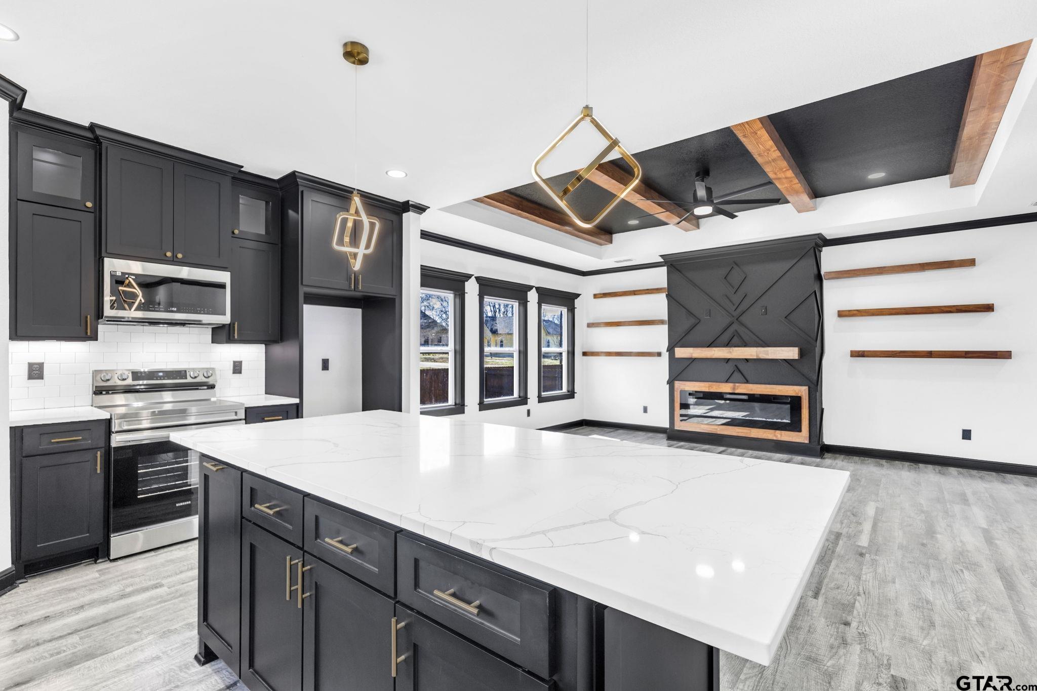 Kitchen with charcoal cabinets, a large white island, and a black fireplace with wood accents.