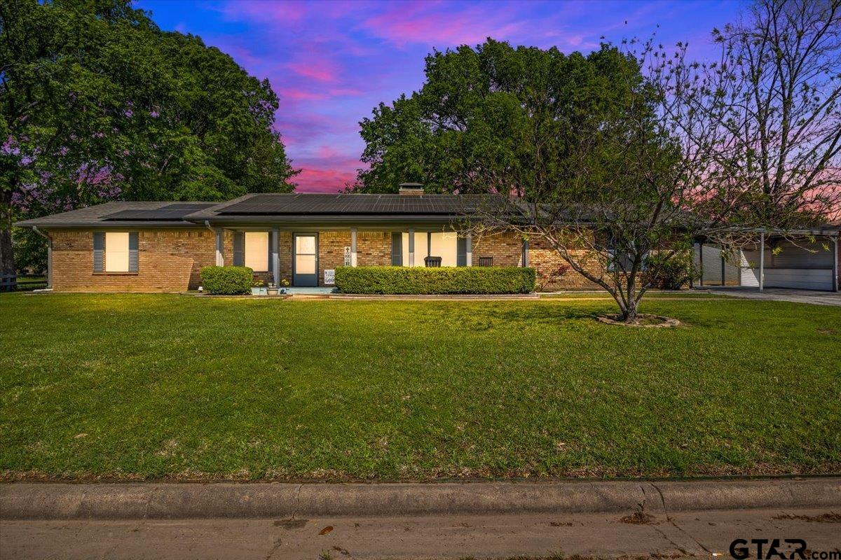 Single-story brick ranch house with rooftop solar panels and a covered carport at dusk.