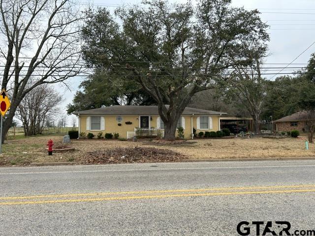 Single-story yellow house with a front porch beneath large mature trees.