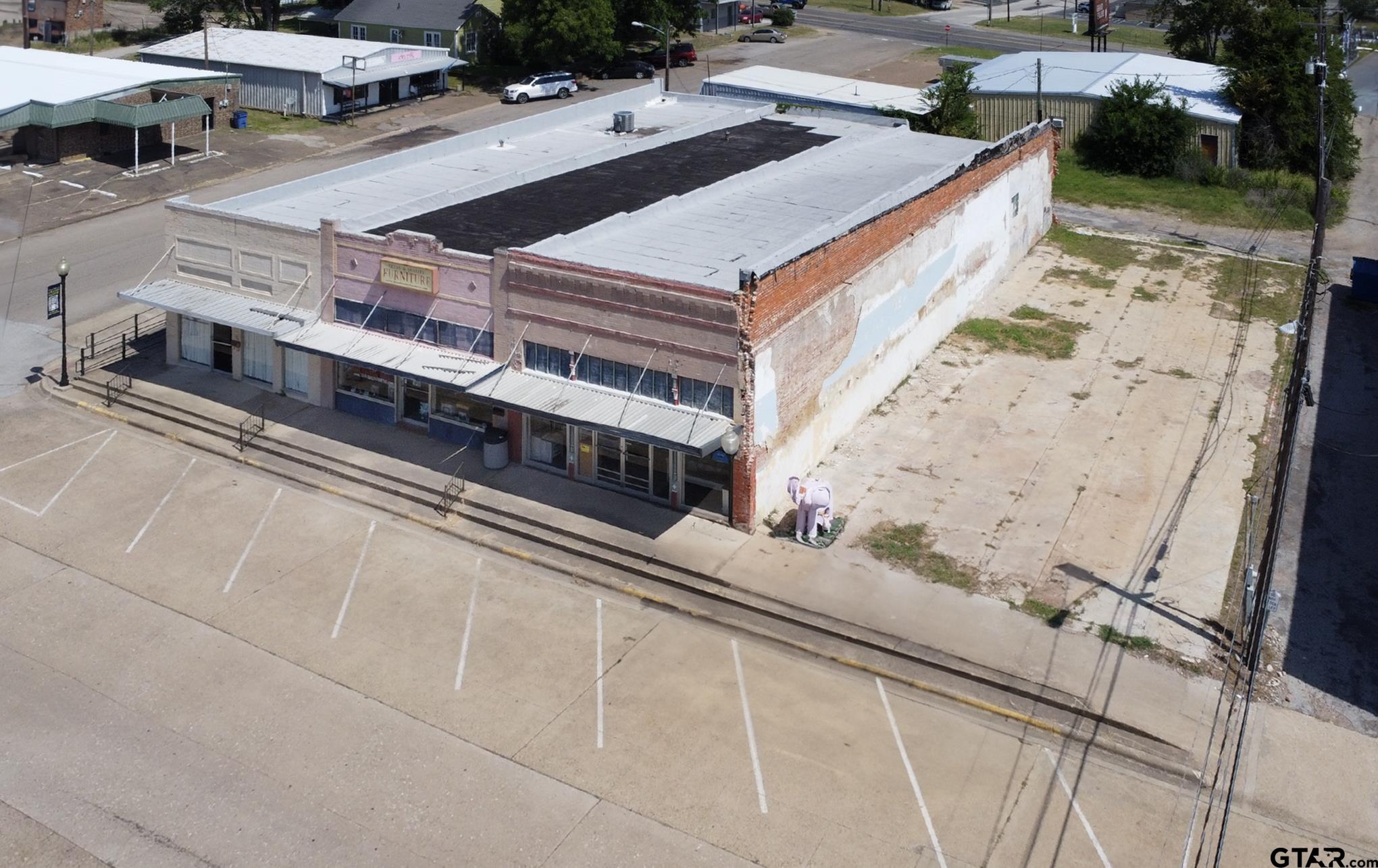 Aerial view of a brick downtown storefront with metal awnings and a broad paved lot.