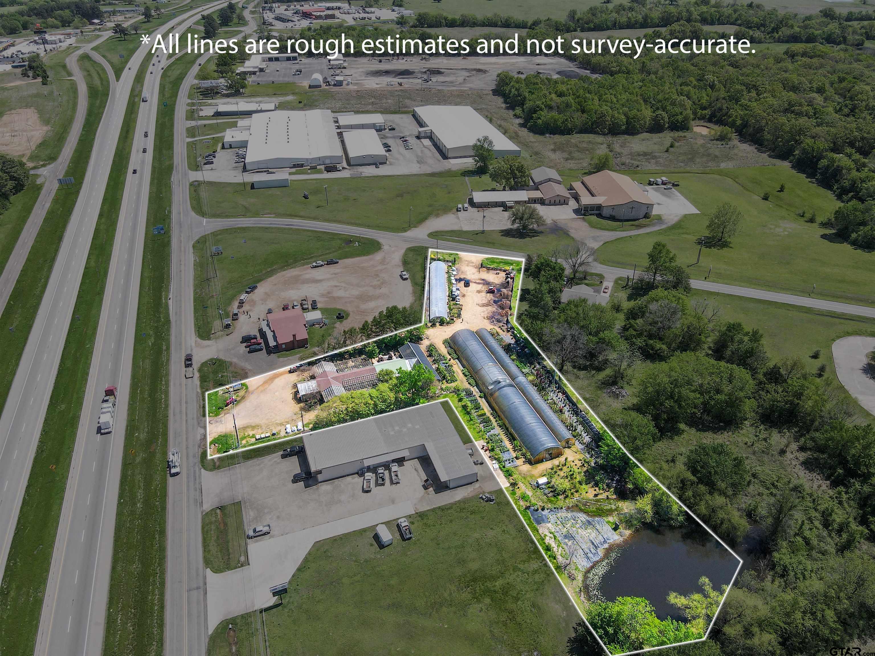 Aerial view of a nursery with greenhouses, growing beds, and a pond, outlined beside a highway.