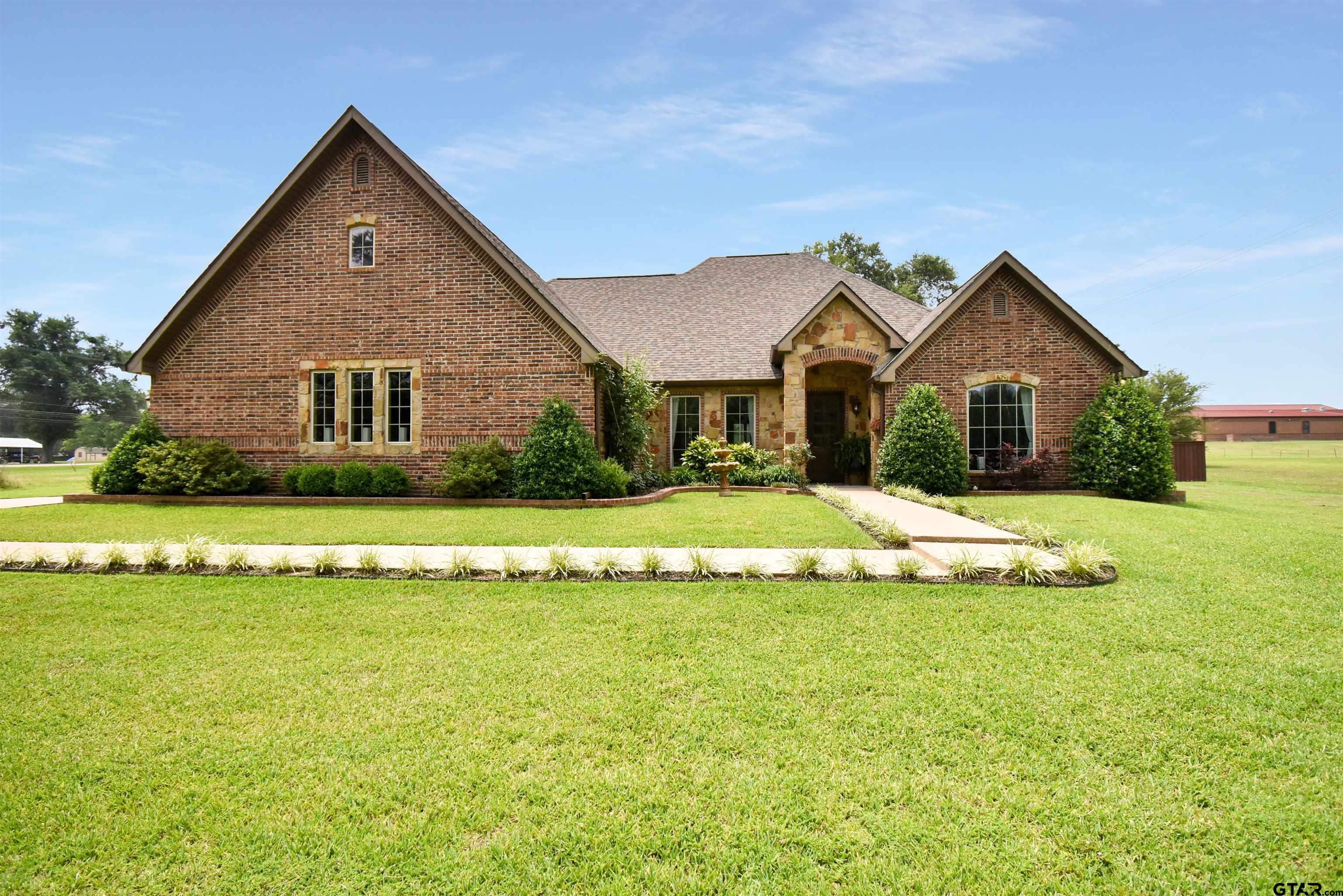 Brick-and-stone house with a gabled roof, landscaped entry, and broad front lawn.