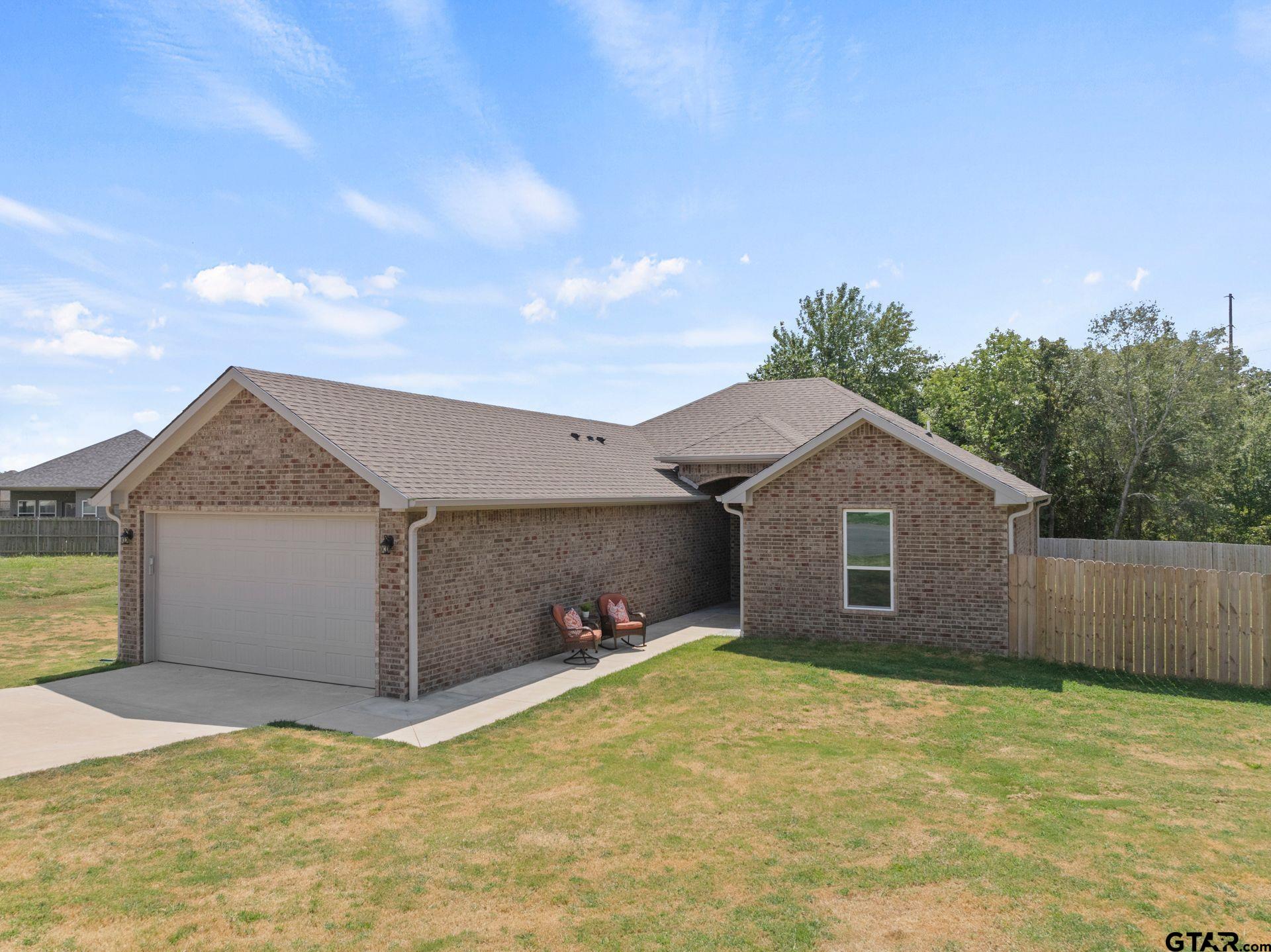 Single-story brick house with a two-car garage, covered entry, and fenced lawn.