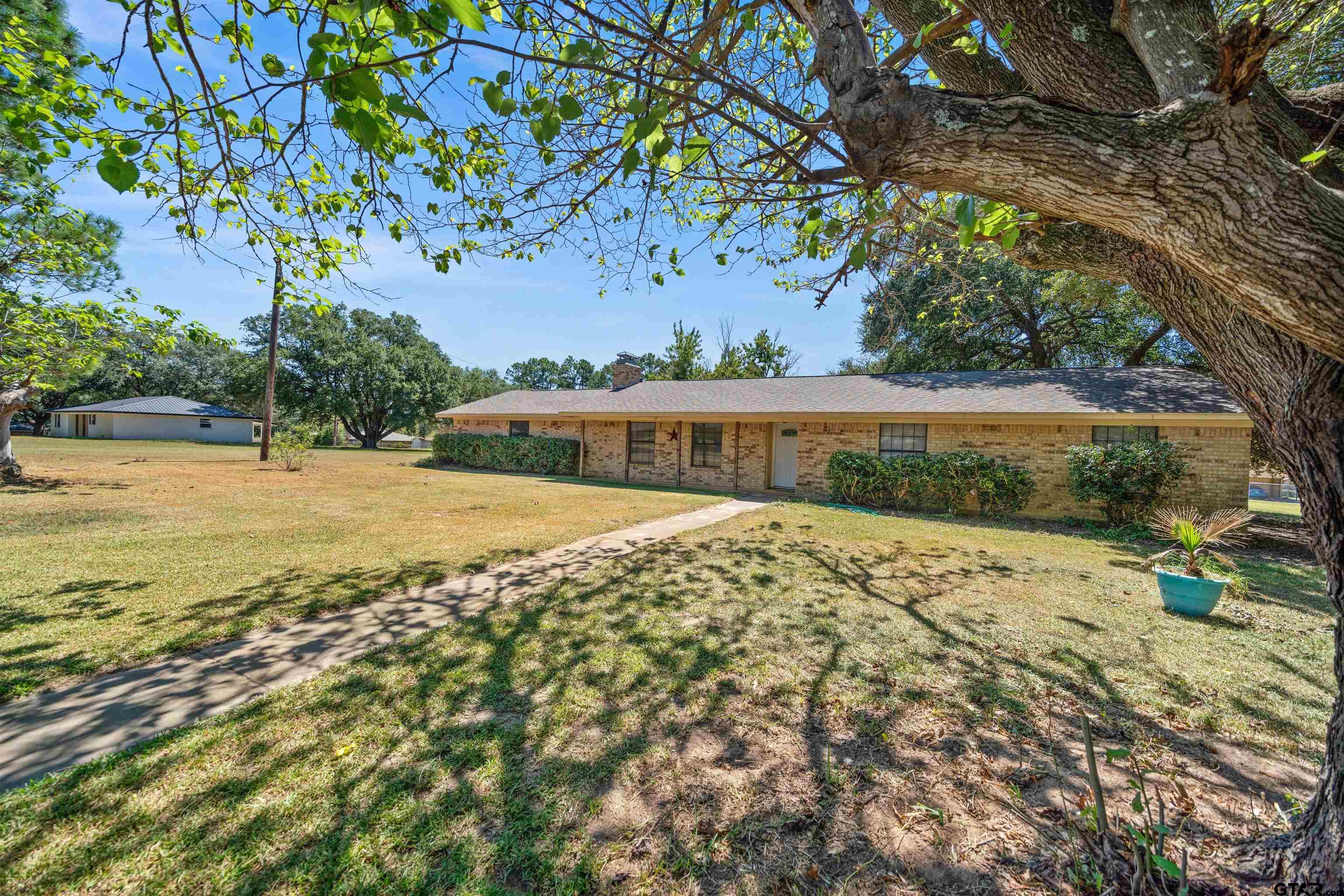 Single-story brick home beneath a large shade tree, with a broad lawn and walkway.
