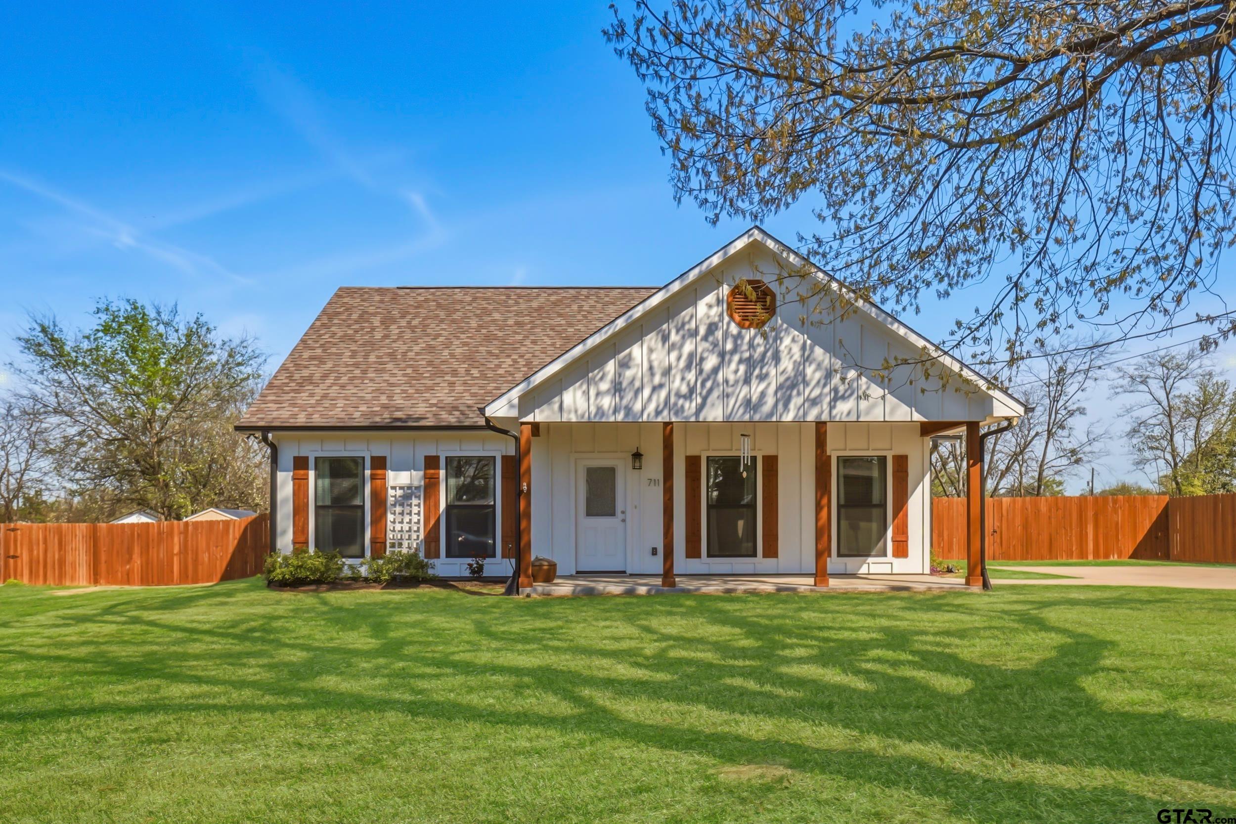 White-sided house with a covered porch, wood accents, and a fenced lawn.