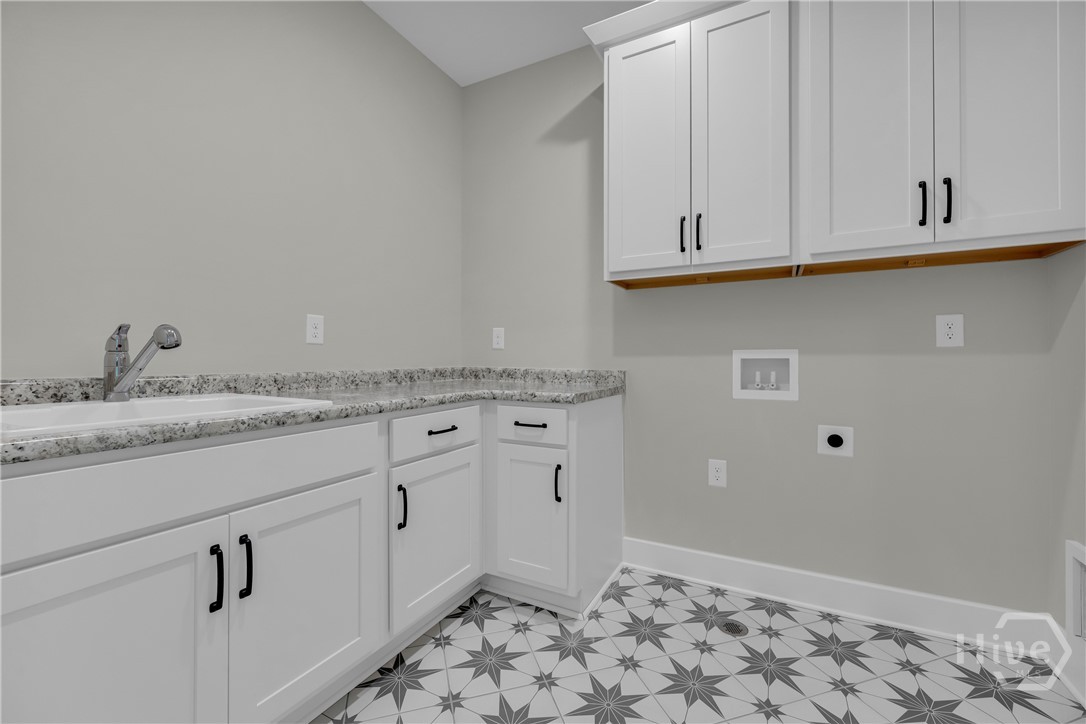 Utility room featuring star-patterned floor tiling, white cabinetry with black hardware, a built-in sink with a pull-down faucet, and ample countertop space