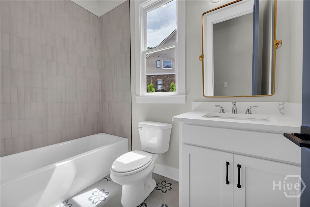Guest Bathroom featuring a white bathtub, gray vertical subway tile surround, white vanity with integrated sink, gold-framed mirror, and patterned floor tiles