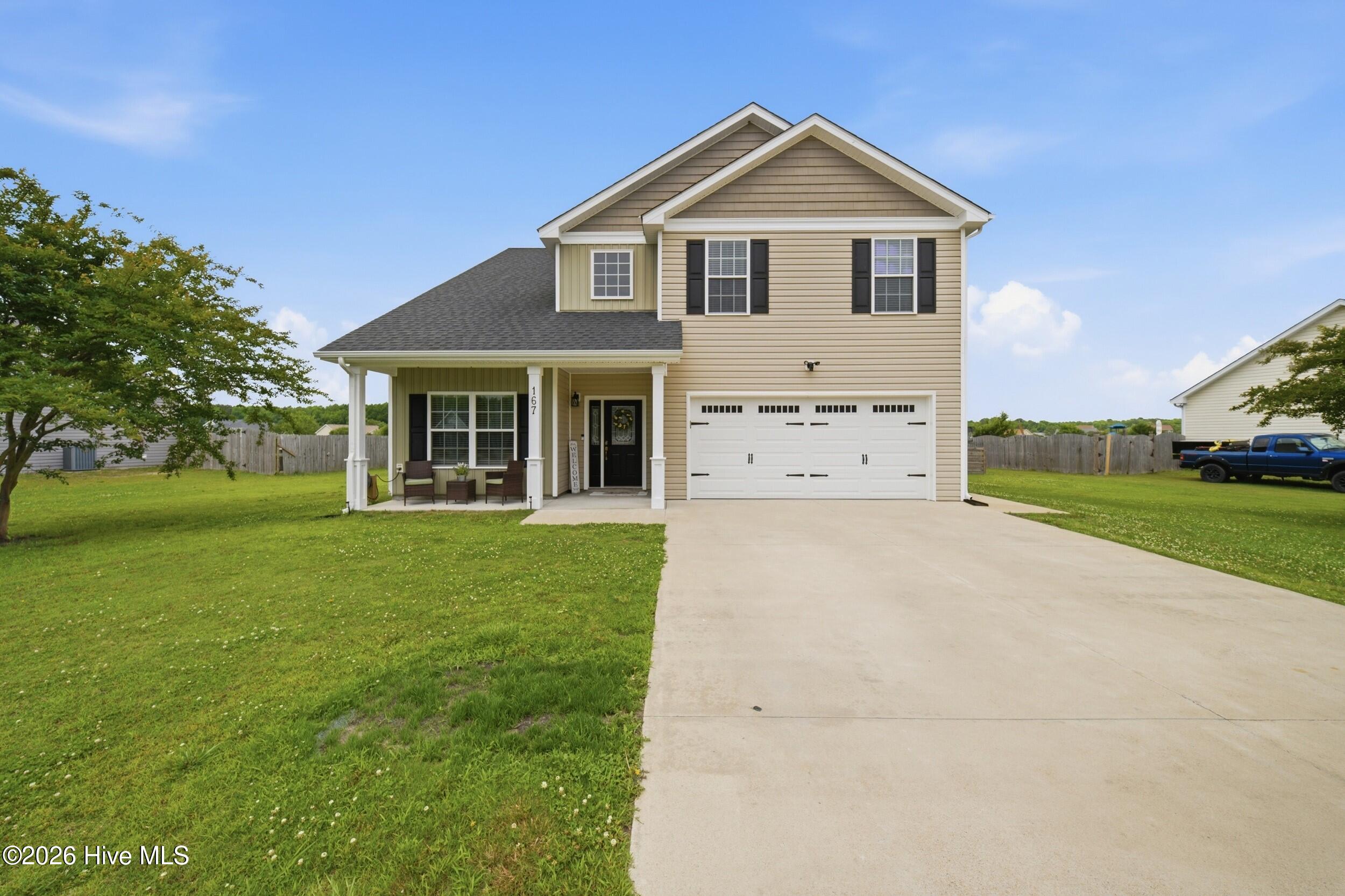 Two-story beige house with a covered porch, double garage, and wide concrete driveway.