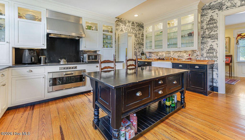 Expanded for modern living, the kitchen features reclaimed heart-pine floors, custom white Shaker cabinetry, glass-front display cabinets, black granite counters, and professional-grade appliances.