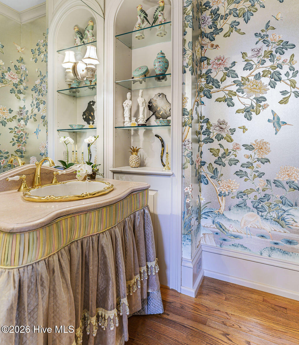 Powder room enveloped in a bespoke, hand-painted silk Chinoiserie mural over a luminous silver-blue ground. Custom vanity topped with premium Tennessee marble. Seamlessly integrated built-in display cabinetry and gold fixtures