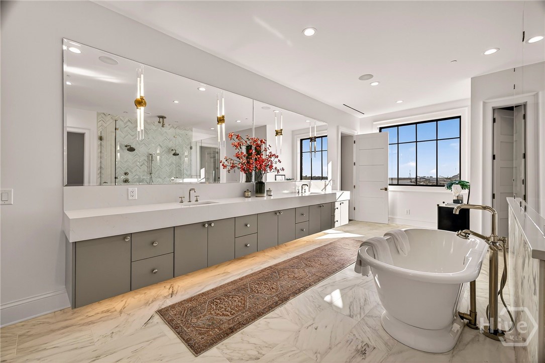 Primary Ensuite with double vanity with freestanding tub and window view. This spa-inspired layout features a long double-sink vanity paired with a freestanding soaking tub, positioned to capture natural light and scenic views. Marble flooring and recessed lighting enhance the sense of volume, while the window placement ensures privacy without sacrificing brightness. A serene retreat designed for daily indulgence.
