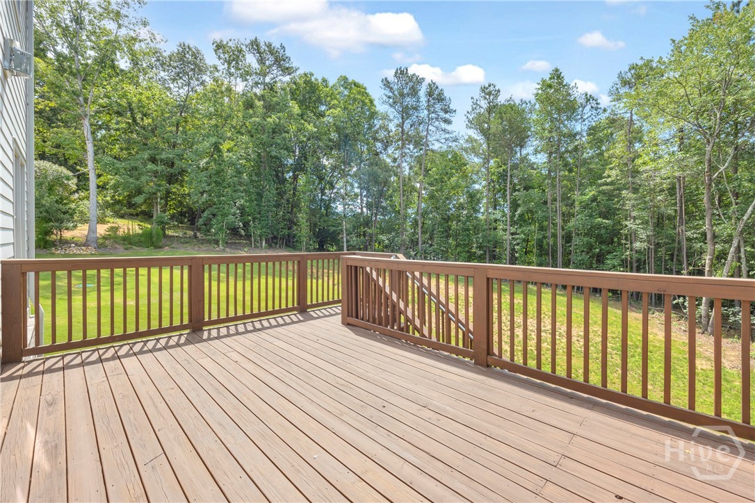 Expansive elevated wood deck with a natural wood finish, featuring a full perimeter railing and a wooded backdrop