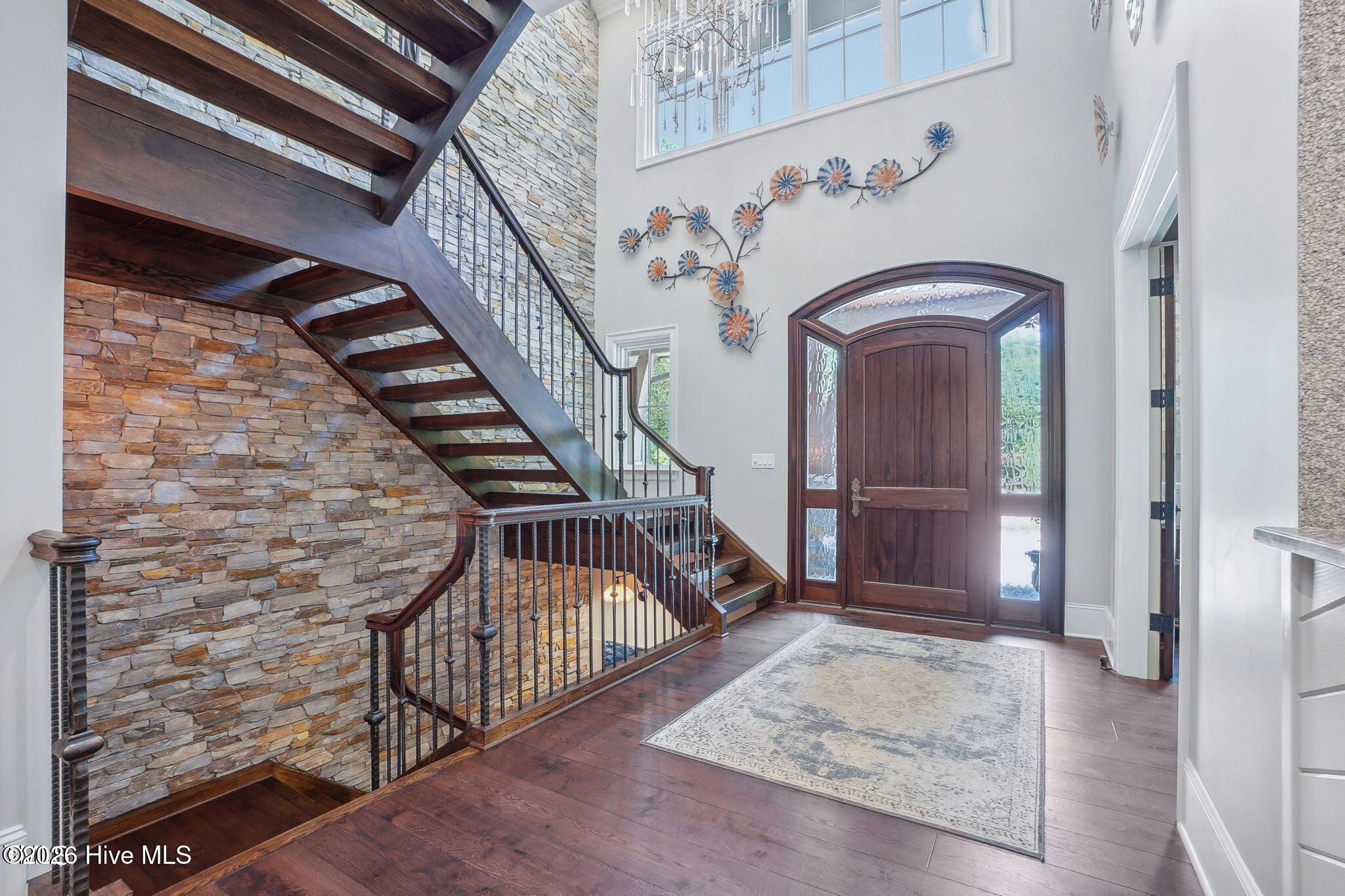 Two story foyer with contemporary lighted staircase and cast iron railing with interior stone accent