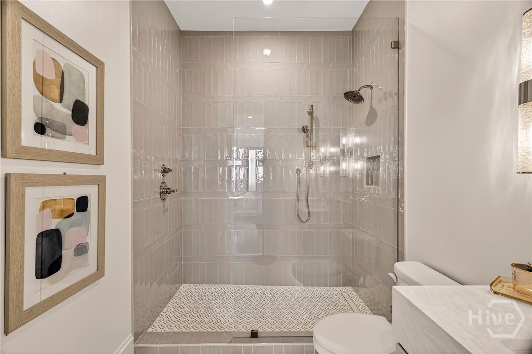 Bedroom 2 Ensuite bath features a walk-in shower with dual showerheads and built-in niches, framed by vertical tilework and marble flooring. A recessed lighting plan and thoughtful wall placement create a perfect serene space.