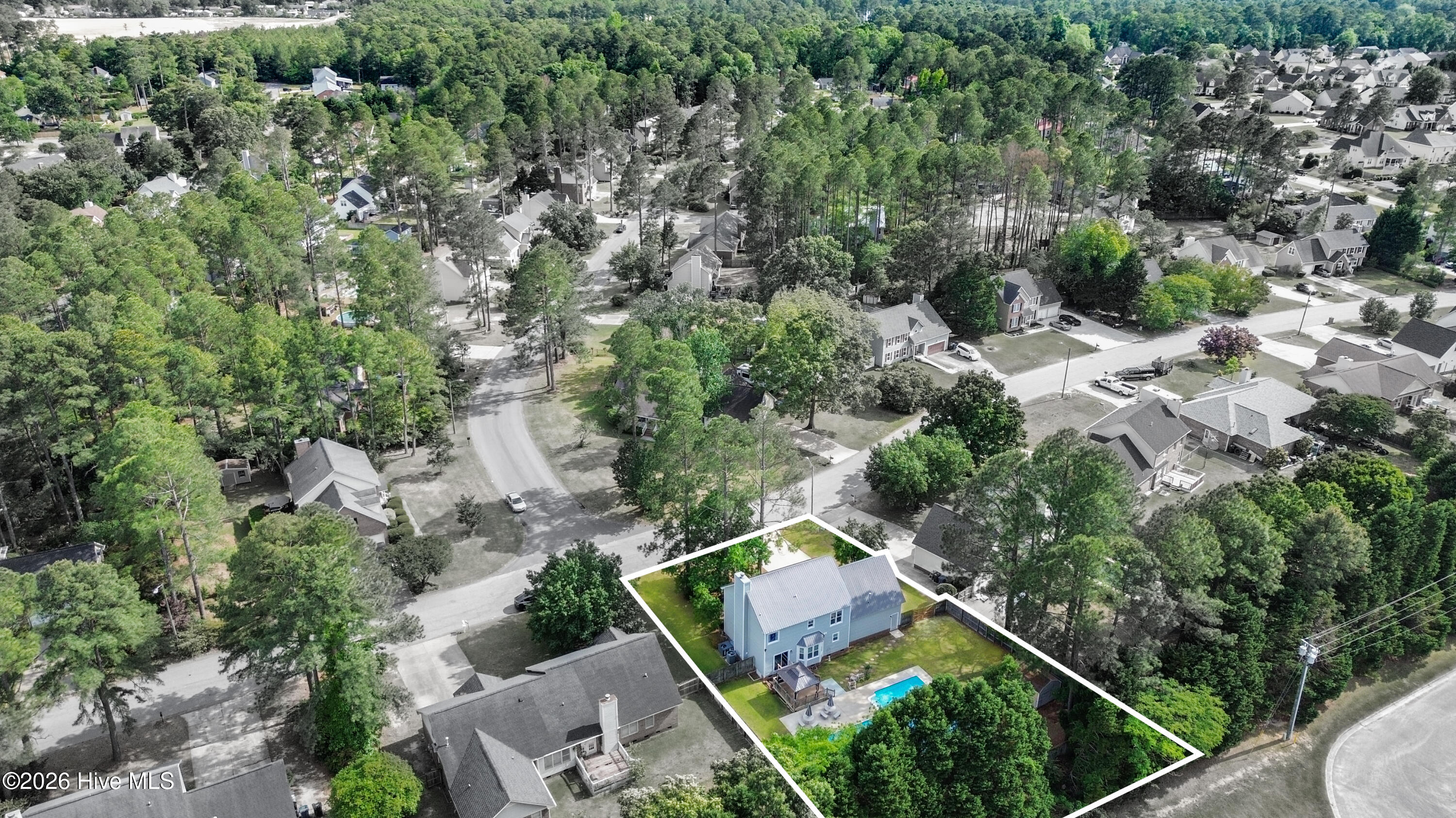 Wide aerial drone perspective highlighting the home’s location within the established Wells Place neighborhood along with the private backyard retreat and pool area. Mature trees and surrounding residential spacing contribute to the property’s peaceful setting and outdoor appeal. Aerial imagery may include approximate property boundary overlays and virtual enhancements for marketing purposes only.