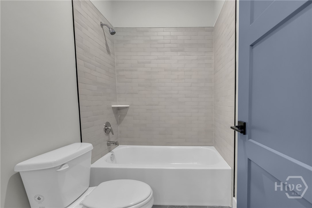 Bathroom featuring a white bathtub, subway tile surround, chrome shower fixtures, and a white toilet