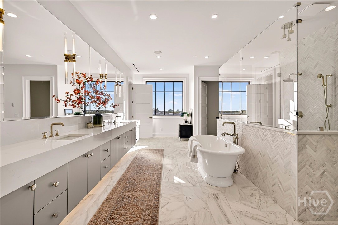 Primary Ensuite unfolds with a balanced layout that integrates dual vanities, a freestanding tub, and a glass-enclosed shower. The shower’s herringbone tile wall adds architectural texture, while the marble flooring and lighting plan create a cohesive, elevated ambiance. A masterfully arranged space for luxury and function.