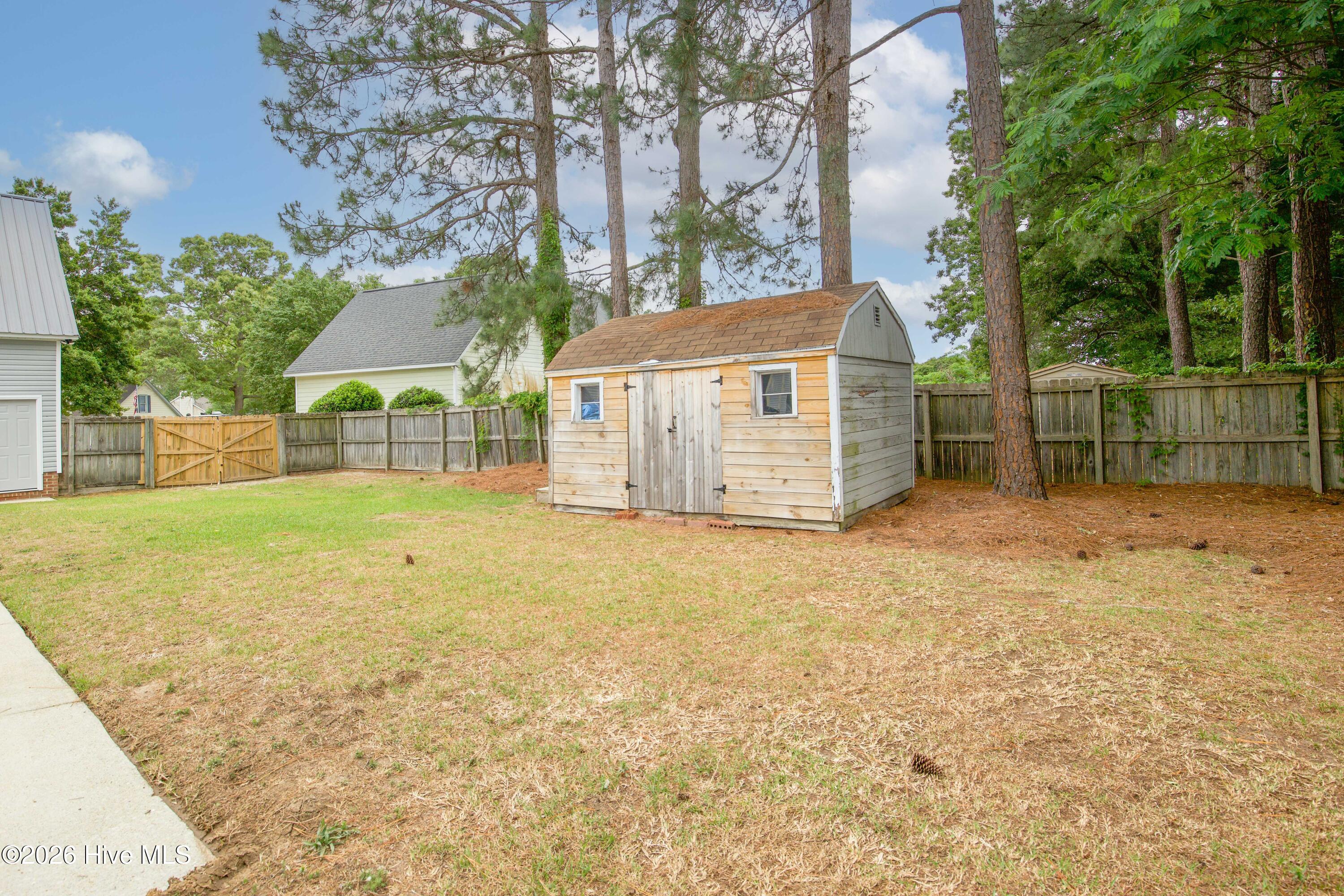 Additional backyard view featuring the detached storage building and spacious fenced yard area surrounding the pool retreat. The storage building offers convenient space for pool supplies, lawn equipment, tools, hobbies, or seasonal storage while preserving usable outdoor entertaining space. Mature trees and established landscaping help create a peaceful backyard environment with added privacy and flexibility.