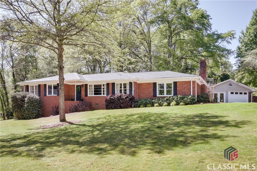 Welcome to 1410 Ivywood Drive, a 1960 brick ranch conveniently tucked away in Oconee County with an Athens address! This charming 3 bedroom, 2 bath home has over 2,000 square feet, is located on a 1.08 acre lot, and includes a detached garage/workshop, large screened porch, and plenty of privacy! This eye-catching home overlooks a large front yard and has plenty of curb appeal with its classic mid-century design and tasteful landscaping. Inside you will enjoy easy, one-level living. The front door opens to a bright living room, and beautiful hardwood floors span most of the home. The living room connects to a dining/flex room and opens to the kitchen and breakfast room. A huge den is right off the kitchen and is anchored by an awesome brick hearth and wood-burning fireplace. Three bedrooms and two bathrooms are located off the hall on the opposite end of the home. Two bedrooms share a full bath with classic white and black tiled walls and a cast iron tub and shower. The primary suite is a welcome retreat and features an enormous bathroom that is simply stunning, with a double vanity, huge window, and attractive mirrors and lighting. The walk-in shower is luxurious with floor to ceiling tile, multiple shower/rainheads, and modern design aesthetics.Outside you’ll enjoy a super spacious screened porch located off the den, with two ceiling fans and a finished concrete floor. A wood deck continues the outdoor living space, and the private backyard contains multiple prolific blueberry bushes and ornamental trees. A detached garage and workshop offer covered parking and a dedicated work space for any craft or hobby, and there is plenty of parking room on the spacious driveway. Need more space? The unfinished basement (with interior access) is clean as a whistle and includes a finished concrete floor and daylight exterior door. The perfect blend of privacy and location is offered in Ivywood. Zoned for Oconee County schools, this home is only 3 miles to downtown Watkinsville, 4 miles to the University of Georgia, 5 miles to Wire Park and 6 miles to Piedmont Hospital-plus Athens Academy is right next door! Don’t sleep on 1410 Ivywood Drive—come see today!