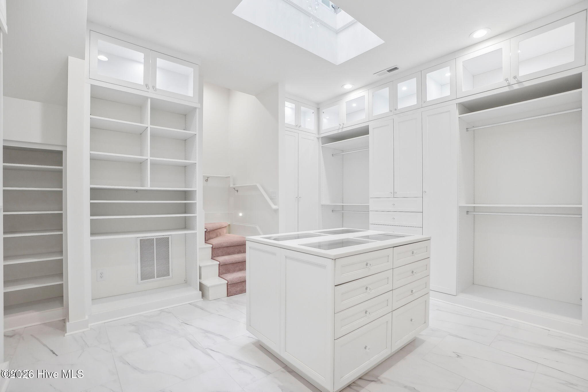 Two story primary closet with custom cabinetry, lighting and two floor chandelier