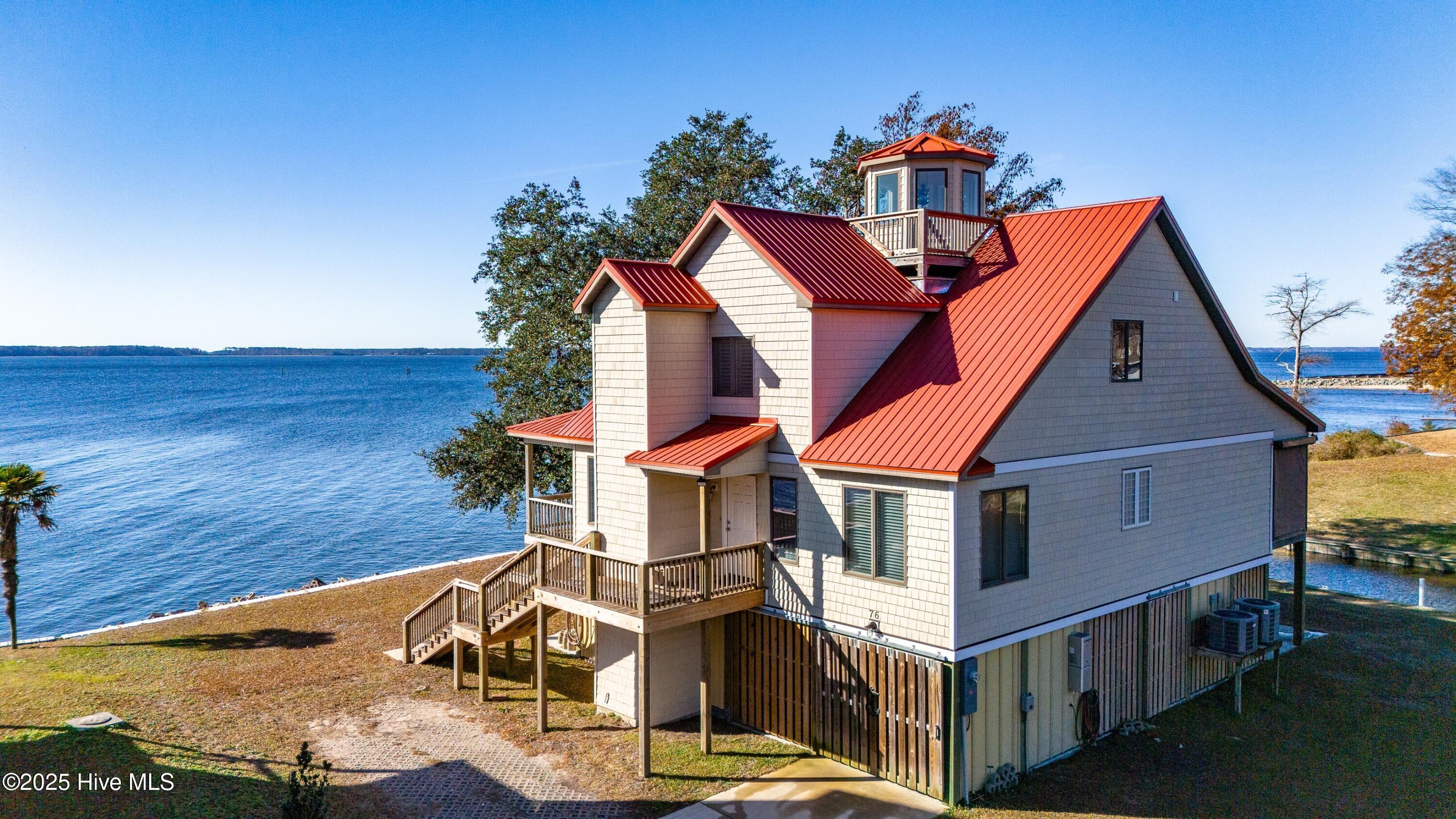 Enjoy iconic coastal living in this Neuse Riverfront home with its distinctive design inspired by the classic Inner Coastal screw-pile cottage-style lighthouses, including the celebrated New Canal Lighthouse on Lake Pontchartrain in New Orleans, Louisiana. Ideally located just a short stroll from the Minnesott Beach Golf & Country Club, minutes from the ferry, and close to Wayfarers Cove Marina, this three-bedroom, 2.5-bath residence blends architectural charm with modern comforts. Elevated on pilings with modular construction, the home features bamboo floors, plantation shutters, Anderson windows, and built-in bookcases that create a warm, character-rich interior. An elevator provides convenient access to all levels. The well-appointed kitchen includes quartz countertops, a JennAir 6-burner cooktop, built-in oven, microwave, refrigerator, dishwasher, and a stackable washer/dryer. Bathrooms include clean, easy-to-maintain walk-in showers. A striking spiral stairwell leads to an upper-level observation platform, offering elevated vistas of the Neuse River and surrounding coastal landscape. Outdoor living continues with a screened porch, open porch, extensive decking, a concrete patio, and a workshop. A two-car garage adds storage and convenience. A metal roof and air-to-air heat pump enhance durability and efficiency. Boaters will love the private boat basin complete with three slips and a 5,000-lb boat lift, providing direct access to the Neuse River. A serene private sandy beach completes this exceptional riverfront setting. A distinctive coastal retreat that beautifully blends lighthouse-inspired architecture with superb waterfront amenities.