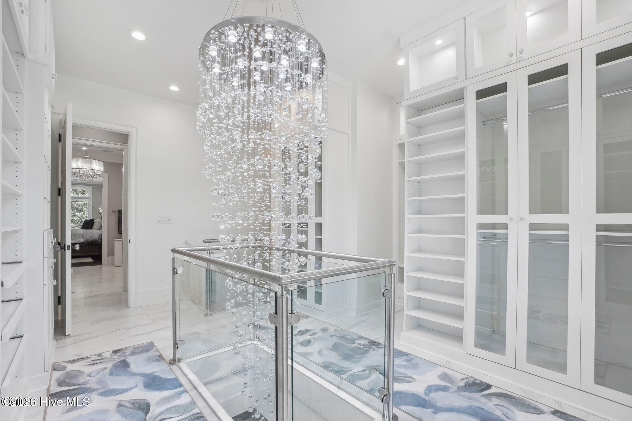 Two story primary closet with custom cabinetry, lighting and two floor chandelier