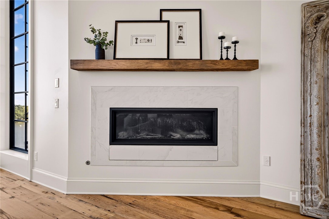 Primary Suite Fireplace wall with carved wood panel and natural light. This architectural vignette features a sleek fireplace framed by marble and a sculptural wood accent, blending modern and rustic elements. Large windows flood the space with natural light, while the layout maintains visual symmetry and warmth. A striking moment of design within the home’s flowing interior.