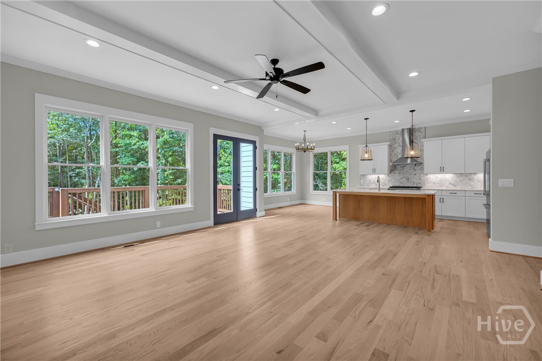 Expansive open-concept room featuring light wood-finish flooring, a tray ceiling with recessed lighting and a ceiling fan, and large windows
