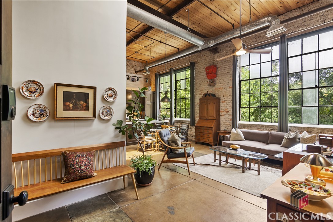 Newly Listed in coveted Whitehall Mill Lofts, an industrial conversion condominium community on the banks of the North Oconee River. Originally the first cotton mill in the Southeast constructed in 1880, Whitehall Mill is an excellent example of adaptive reuse of historic buildings for residential use. Unit 508, one of few ONE LEVEL condominiums, has been artfully renovated from top to bottom. Upon entry, there is an abundance of natural lighting from the skylight and original wrought iron windows. Stained concrete floors run throughout the unit. An open concept floor plan is perfect for entertaining, and the 15' high ceilings with exposed beams allow the space to feel even more spacious. A gourmet kitchen awaits with custom cabinetry, tile backsplash, built-in pantry, natural quartzite countertops, integrated high-end refrigerator and dishwasher, plus a six burner ZLine oven. Enjoy views of the river while you prepare meals and entertain guests! Remote controlled solar shades in the living room and kitchen as well as smart technology for speakers, lighting, and doorbell are just added bonuses. The primary suite is spacious and features an exposed brick wall and an ensuite bathroom with tiled shower with stain resistant glass door, high-end, self-cleaning Japanese toilet with heated seats, and reclaimed wood vanity. Off the kitchen is the second bedroom or studio space/ office with large closet, exposed brick, and TV mount above a shiplap wall feature. A half-bathroom features an in-wall toilet, tile flooring, and high end features. Residents of Whitehall Mill Lofts may enjoy the use of the fire pit, outdoor grilling areas, river access, and walking trails.