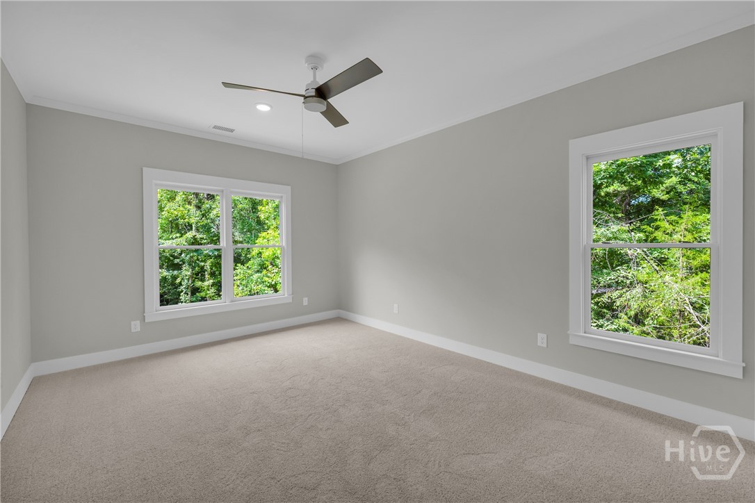 Spacious room featuring neutral carpeting, light gray walls, white trim, and a ceiling fan with integrated lighting
