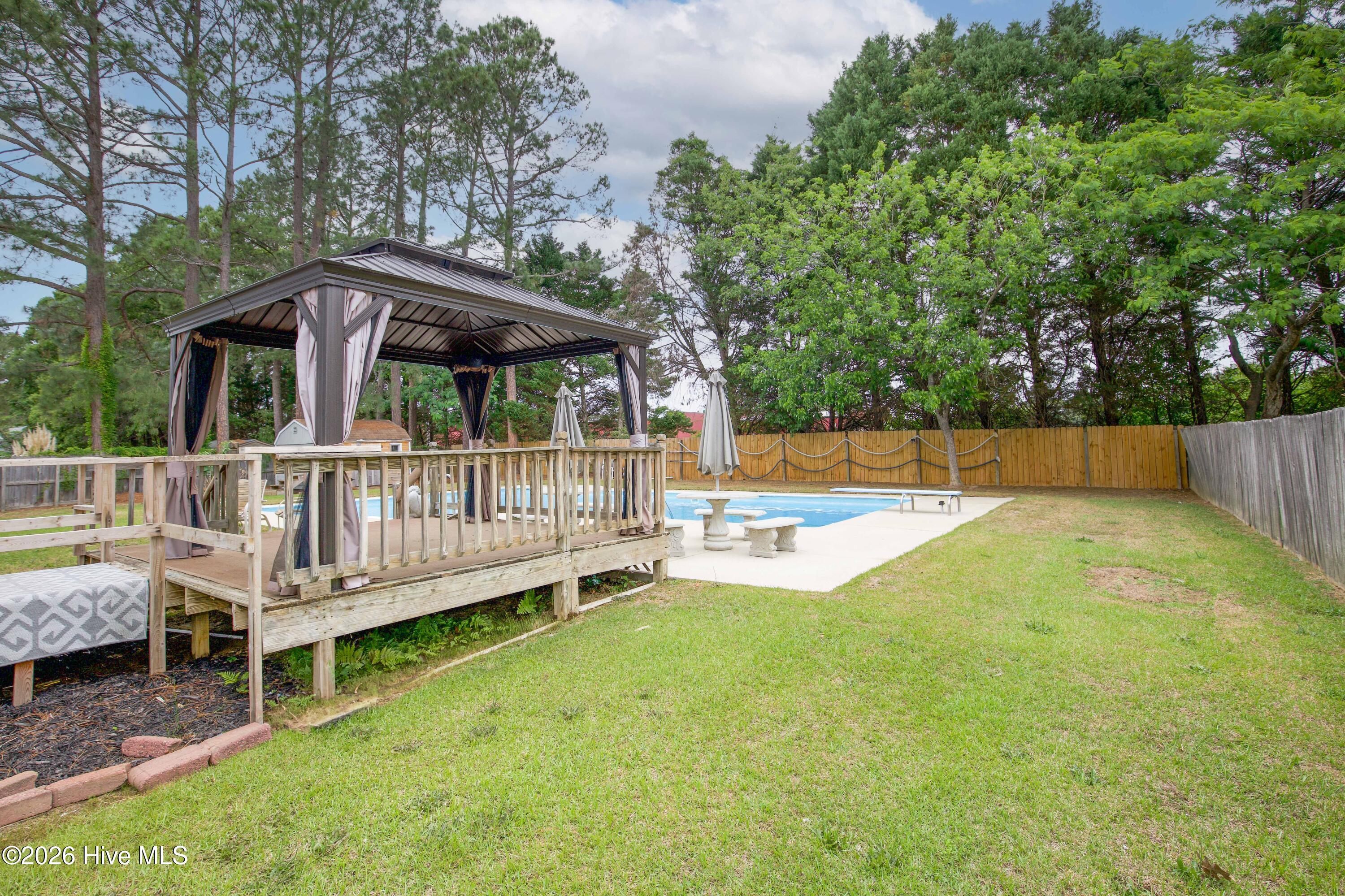 Wide backyard view showcasing the covered gazebo, elevated deck, pool area, and fenced outdoor living space. Designed for entertaining and everyday enjoyment, this backyard retreat combines privacy, functionality, and lifestyle appeal in one complete package. Located in the established Wells Place community near Fort Bragg, shopping, dining, schools, and the Fayetteville VA Health Care Center, this home offers a rare combination of location, outdoor amenities, and no HOA restrictions.