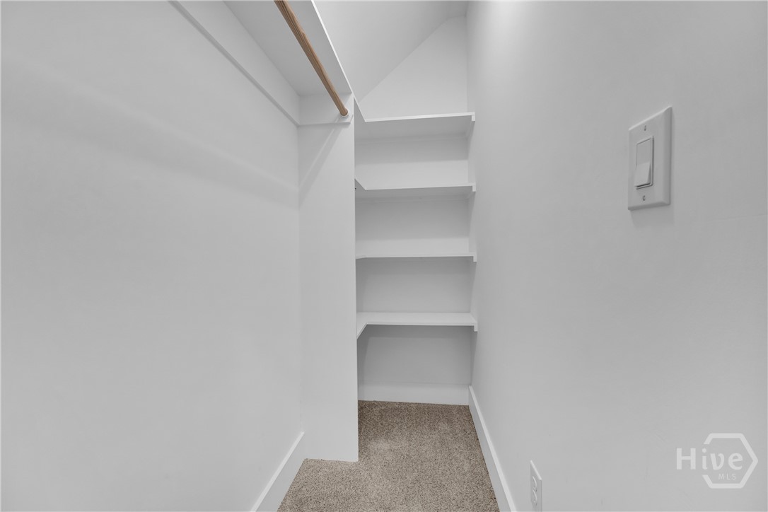 Secret Passageway in Walk-in closet featuring built-in shelving, a clothes rod, light neutral wall paint, and beige carpeting