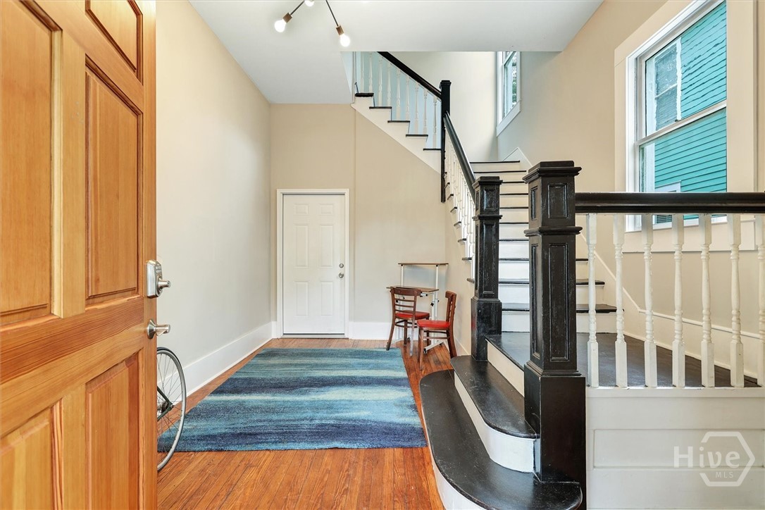 Bright entry foyer featuring hardwood floors, high ceilings, and a staircase with classic railing details.