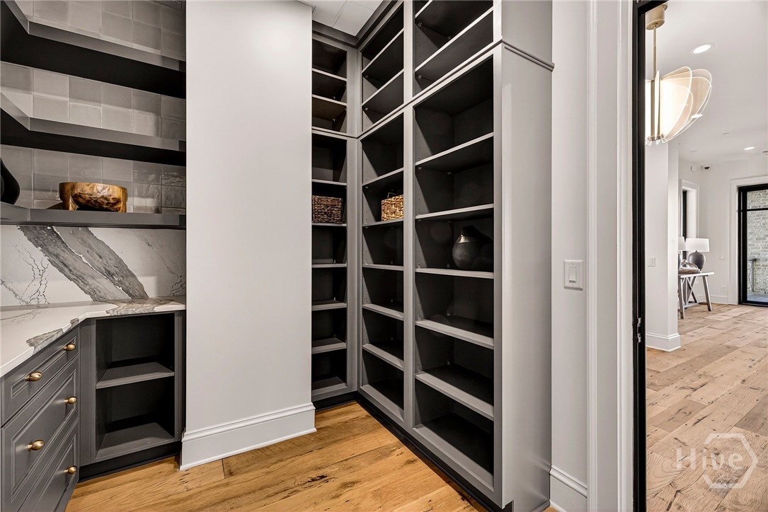 L-shaped pantry with marble counters and hallway connection. An expansive L-shaped pantry offers floor-to-ceiling storage and seamless connection to adjacent living areas. Marble countertops and integrated cabinetry enhance the space’s utility, while the open hallway transition maintains architectural cohesion. Designed for elegant organization and effortless flow.