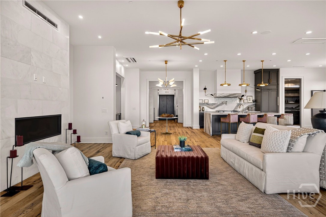 Open-concept living and kitchen. A seamless open-concept layout connects the living area to the chef’s kitchen with architectural grace. The marble fireplace serves as a central anchor, while warm wood flooring and recessed lighting guide the eye through expansive, light-filled zones. Ideal for elegant entertaining and effortless daily living.